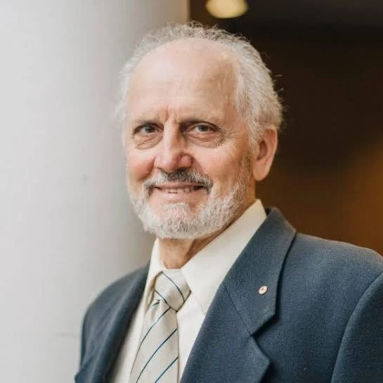 Portrait of George Paxinos, smiling, with white hair and a beard, wearing a navy blazer and striped tie